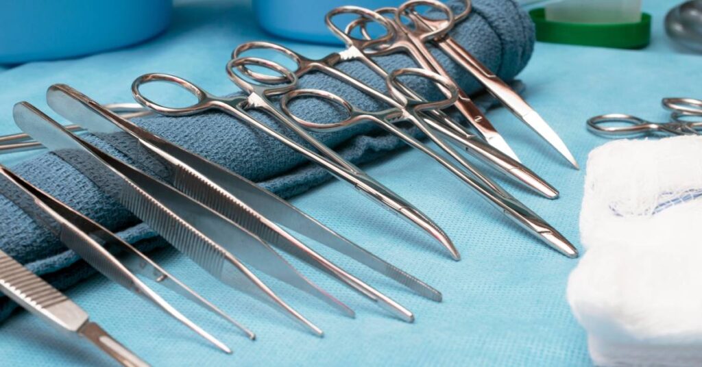 A collection of metal surgical instruments, including tweezers, scissors, and scalpels, lie against a clean, rolled up towel.