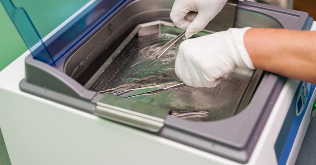 A medical professional placing tweezers and other metal tools in an ultrasonic cleaner for sanitation.