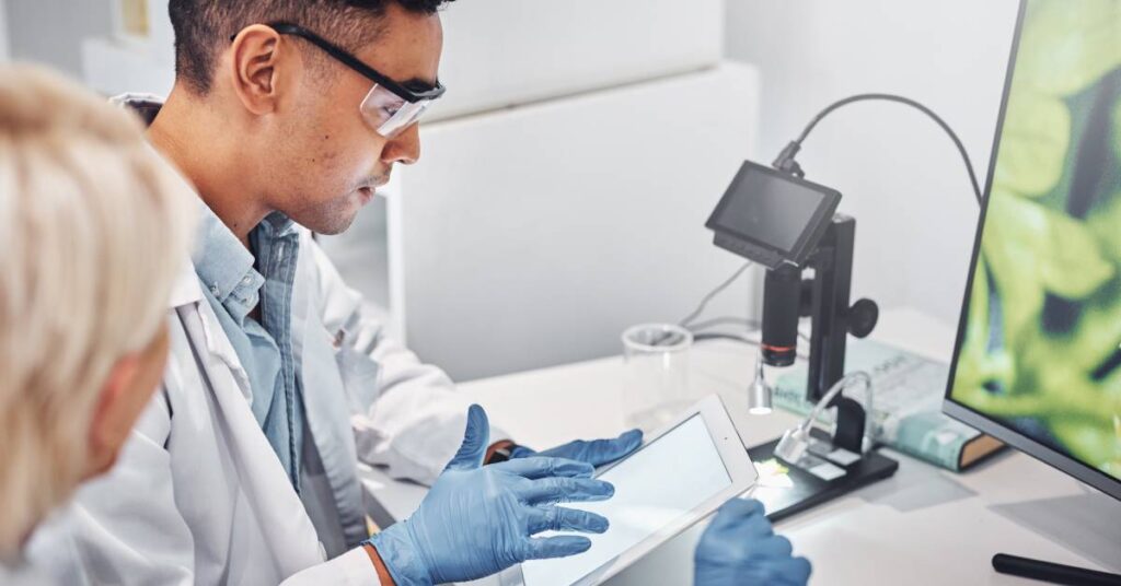 A pair of medical professionals sitting at the same desk. They are looking at a computer and a tablet together.