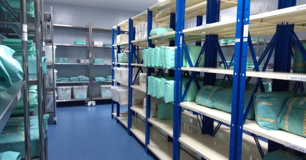 Storage shelves full of medical devices in sterile packaging. Most are wrapped, but some are in rigid sterilization containers.