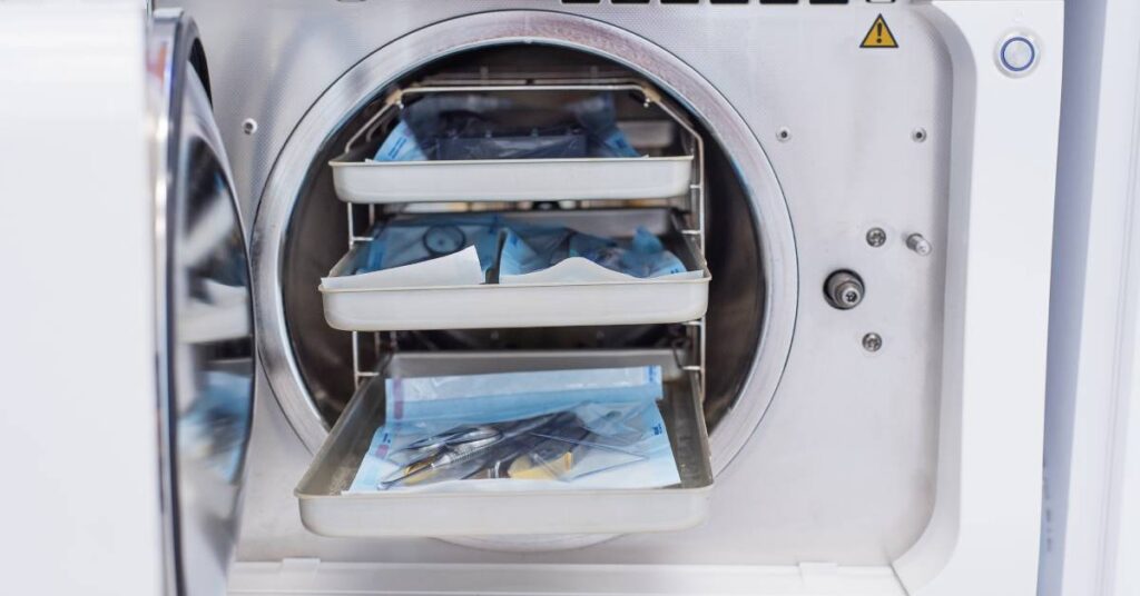 Three trays of wrapped medical instruments going into an autoclave for disinfection and sterilization.