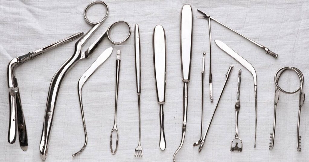 A row of clean metal medical instruments, including forceps, tweezers, and more, lined up on a white cloth.