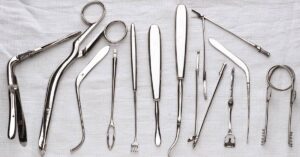 A row of clean metal medical instruments, including forceps, tweezers, and more, lined up on a white cloth.