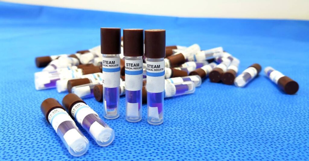 A small pile of biological indicator vials labelled for a steam sterilization process. They are lying on a blue surface.