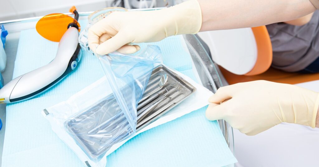 A healthcare professional wearing gloves and opening a sterilization pouch containing a tray of dental tools.
