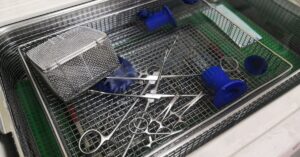 Medical instruments sitting in a wire tray. The tray rests within an ultrasonic cleaning machine.