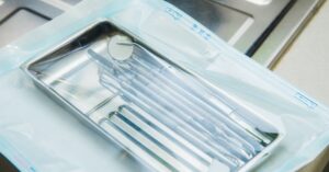 A metal tray of handheld dental instruments wrapped in a semi-transparent sterilization pouch.