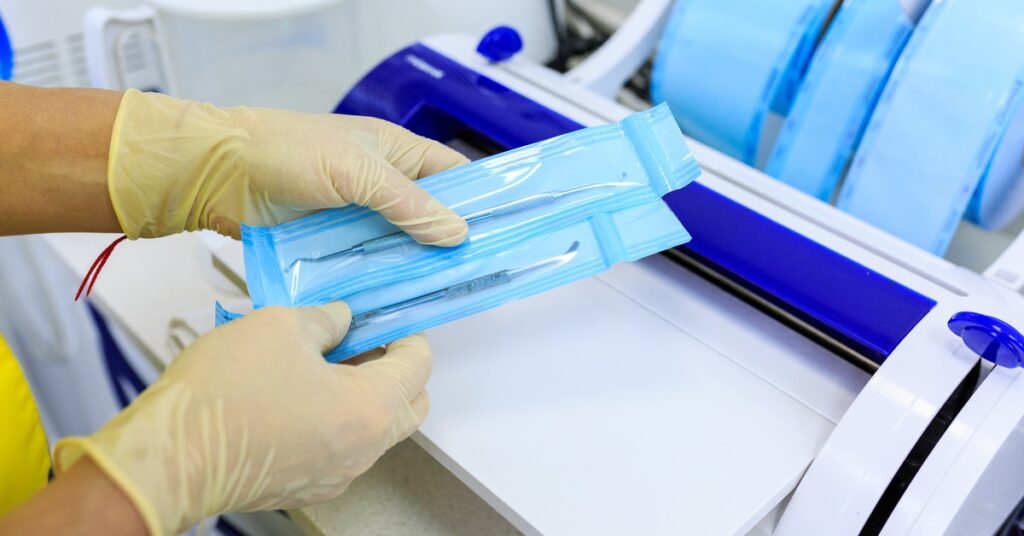 A person wearing gloves and holding two medical instruments sealed in sterilized medical device packaging.