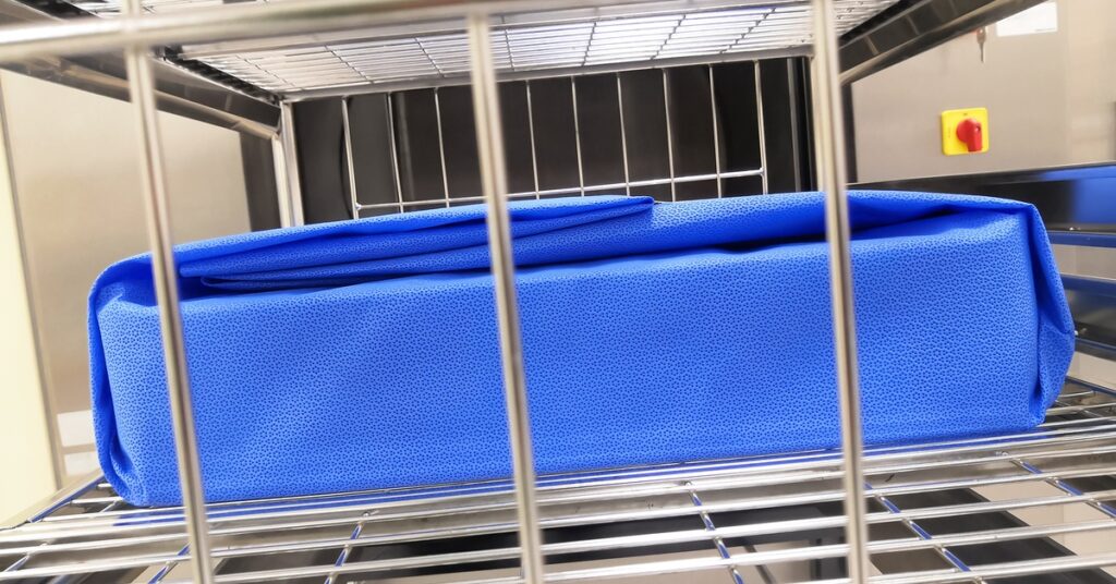 A blue sterilization wrap around a rectangular container set in the wire rack of a sterilization machine.