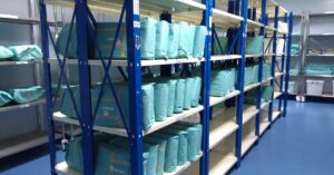 Shelves in a storage room full of medical devices packaged in sterilization wraps, rigid containers, and other packaging types.
