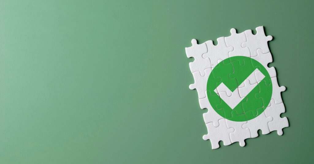 Puzzle pieces come together on a green background to create a white checkmark in a green circle on a white background.
