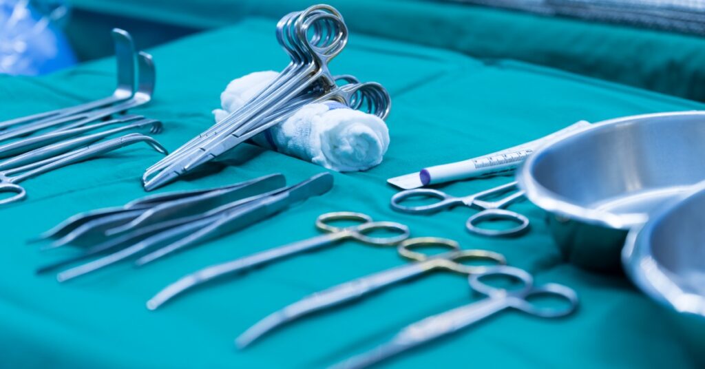 Stainless steel forceps, clamps, retractors, and other surgical instruments are on a surgical drape beside rolled gauze.